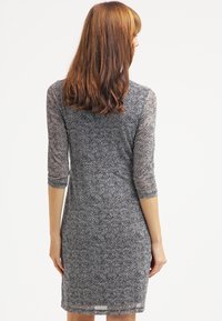 Svart och vit mönstrad figurnära klänning med trekvartsärmar, slät textur, knälång längd och rundad halsringning.