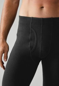 Sous-vêtements longs noirs à côtes avec un design ajusté, présentant une poche moulante et une ceinture élastique. La texture est lisse et bien ajustée.