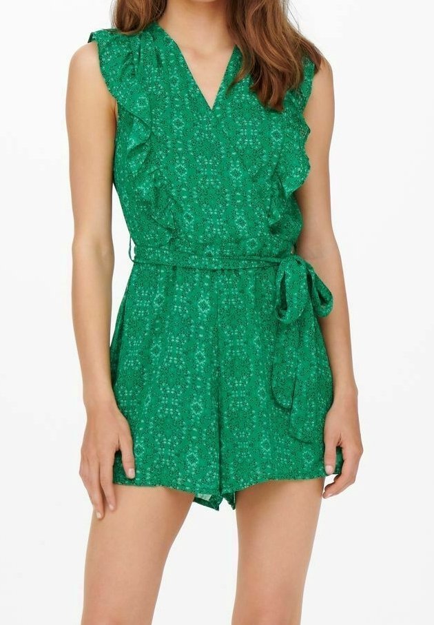Femme portant une combinaison-short verte à motifs sans manches avec des épaules volantées et une ceinture nouée à la taille.