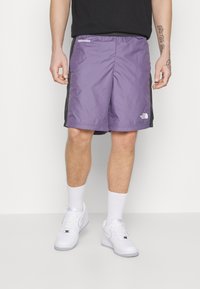 Fialové sportovní kraťasy s černými bočními panely, lehký materiál, elastický pas a malé logo na levé nohavici. Kombinované s bílými teniskami.