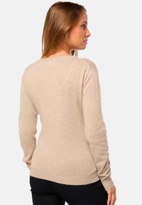 Pull en beige à manches longues en matière douce. Il présente un col rond et un ourlet côtelé. Il a une coupe ajustée avec une texture lisse.