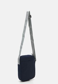 Borsa a tracolla in tessuto navy con una texture morbida, tracolla grigia regolabile, chiusura con zip e design minimalista.