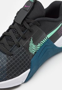 Black athletic shoe with a textured upper, mesh design, and teal accents. Features a prominent swoosh and a rubber outsole with grip patterns.