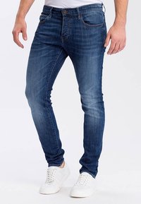 Dark blue slim-fit jeans with a faded wash, five pockets, and belt loops, paired with white sneakers and a plain white t-shirt.