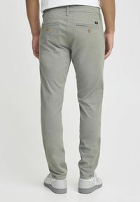 Lichtgrijze broek met een slim fit, twee achterzakken met ronde oranje knopen en een geweven label boven de rechterzak.