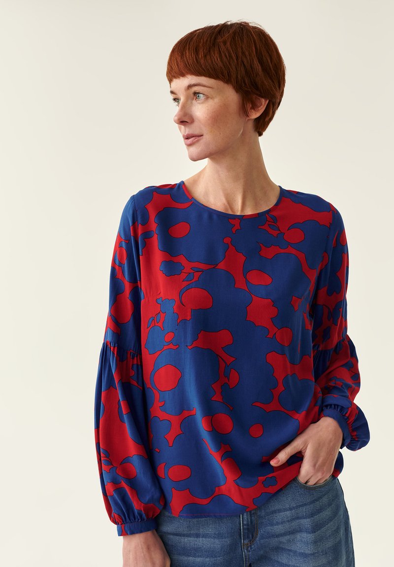 Blå bluse med en dristig rød blomstermønster, rund udskæring og lange pufærmer. Letvægtsstof der falder blødt. Kombineret med denim.