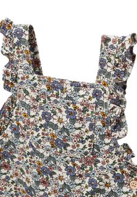 Salopette fleurie, présentant des fleurs bleues, roses et jaunes sur un fond blanc, bretelles à volants et détail de poche avant.
