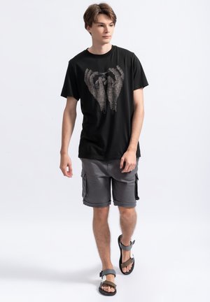 Zwarte katoenen t-shirt met een gedetailleerde handenafbeelding, gecombineerd met grijze cargo shorts en zwarte sandalen met verstelbare banden.