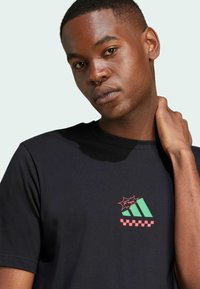 Maglietta nera in cotone con una piccola grafica rossa e verde con forme geometriche e motivo a scacchi sulla parte sinistra del petto.