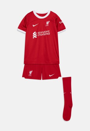 Kit da calcio giovanile del Liverpool FC che presenta una maglia rossa con dettagli bianchi, pantaloni corti rossi abbinati e calze rosse, il tutto realizzato in materiale traspirante.