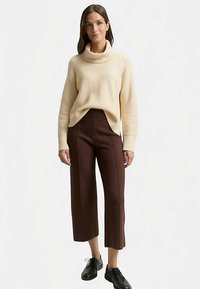 Pull à col roulé côtelé crème associé à un pantalon marron à jambes larges et taille haute, avec détails de coutures verticales. Le mannequin porte des chaussures noires.