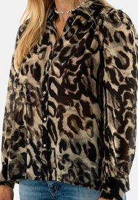 Blusa transparente con estampado animal en negro y beige, de manga larga, con cuello clásico y cierre de botones en la parte frontal. Detalle de tejido texturizado.