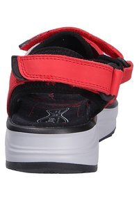 Red sandal with adjustable straps, black interior padding, cushioned sole, and white rubber outsole. Features a hook-and-loop fastening.