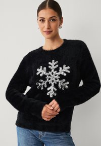 Zwarte, pluizige trui met een groot glinsterend sneeuwvlokontwerp. Zachte textuur, lange mouwen en een ronde halslijn. Casual pasvorm.