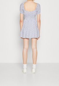 Bílé šaty s květinovým potiskem, krátkými nabíranými rukávy, čtveratým výstřihem na zádech a elastickým pasem. Nosené s bílými teniskami a ponožkami do kotníků.