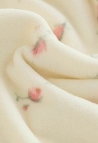 Fleece deka s měkkou, hladkou texturou; krémová základní barva s malými růžovými květinovými vzory a zelenými akcenty.