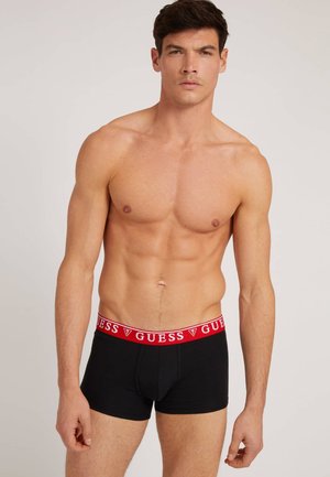Schwarze Boxer-Briefs mit einem roten Logo-Taillenbund "GUESS"; enganliegendes Design, Baumwollmaterial, glatte Textur und keine sichtbaren Muster.