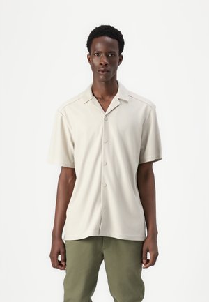 Short-sleeve, light beige collared shirt with a textured pattern, featuring a button front and relaxed fit, paired with olive green pants.