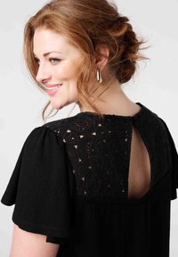 Robe noire avec de courtes manches bouffantes et un dos en dentelle audacieux avec des motifs circulaires. Encolure ronde avec une ouverture en forme de clé à l'arrière.
