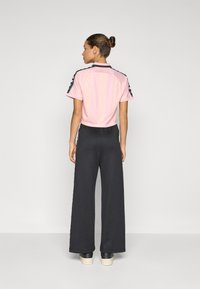 Camisa curta rosa com acabamento nos ombros, emparelhada com calças largas pretas. Tecido suave, design simples e detalhes de hardware mínimos.