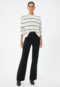 Pull en knitted blanc avec des rayures noires horizontales, associé à un pantalon large noir taille haute et des bottes à talons noires.