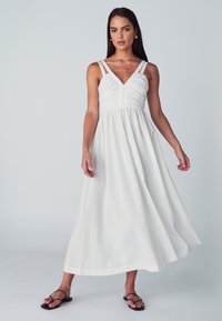 Hvid maxikjole med justerbare dobbelte stropper, rynket krop, skørt med vidde, lavet af letvægtsstof, har en glat tekstur og ankellængde.