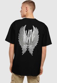 Sort bomulds t-shirt med stort hvidt vingegrafik, hvor "HOPE"-teksten er centreret ovenfor og "THE GUIDING LIGHT" nedenfor, afslappet pasform.