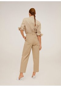 Chemise beige légère à manches retroussées, associée à un pantalon large beige taille haute et des chaussures à talons hauts blanches.