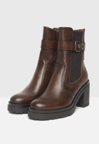 Bottines en cuir marron avec un talon carré, dotées de panneaux élastiques sur les côtés, d'une boucle en accent et de semelles en caoutchouc texturé.