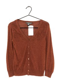 Cardigan rouille à boutons avec manches longues et détail en dentelle près des épaules, suspendu à un cintre en fil noir avec une étiquette blanche.