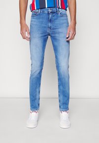 Jeans de denim ajustados en azul claro con una textura suave, diseño de cinco bolsillos y un ligero desvanecimiento. Combinados con zapatillas blancas.