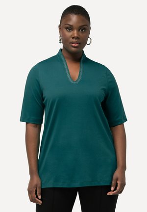 Top verde smeraldo a maniche corte con scollatura a V, caratterizzato da eleganti decorazioni. Tessuto morbido e vestibilità ampia, abbinato a pantaloni neri.