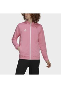 Rosa treningsjakke med høy krage, hel glidelås og ribbestrikkede ermer. Har et hvitt Adidas-logo og er laget av glatt, lett stoff.