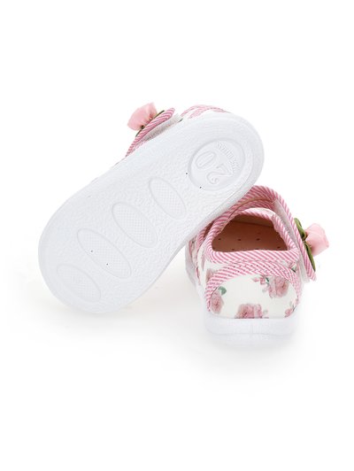 Zapatos infantiles con suela de goma blanca, parte superior de tela floral, acentos en rosa y una flor decorativa en la tira.