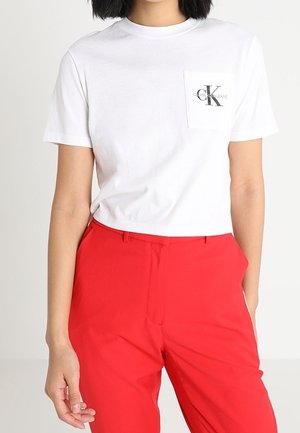 Biała bawełniana koszulka z kieszonką na lewej piersi z czarnym logo. W zestawieniu z czerwonymi, dopasowanymi spodniami, prezentującymi jednolite kolory i prosty design.