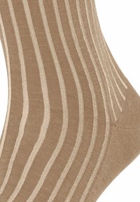 Beige sokker med ribbet tekstur, der har skiftevis mørkere og lysere stribede mønstre, som viser et glat strikkedesign.