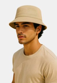 Beiger Sonnenhut aus Baumwolle mit breiter Krempe. Das Modell trägt ein hellbeiges T-Shirt, das eine glatte Textur und ein schlichtes Design zeigt.