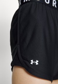 Svarta atletiska shorts med en figursydd design, tillverkade av texturerat tyg. Har en vit logotypdetalj och ett midjeband med texten "ARMOUR".