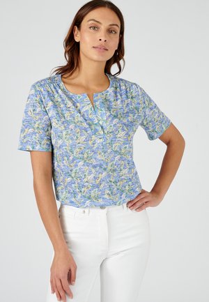 Blouse à manches courtes en tissu bleu clair avec un motif floral feuillu. Dispose d'un col rond et d'un léger froncé aux épaules.