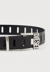 Μαύρη συνθετική ζώνη με ασημένιες μεταλλικές λεπτομέρειες, διαθέτει ρυθμιζόμενες τρύπες και έντονο λογότυπο "DIESEL" στην αγκράφα.