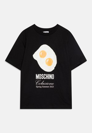 Juodas medvilnės marškinėlis su geltona ir balta grafika, vaizduojančia keptą kiaušinį, su užrašu "Moschino Colazione Pavasaris Vasarą 2025" baltu tekstu.