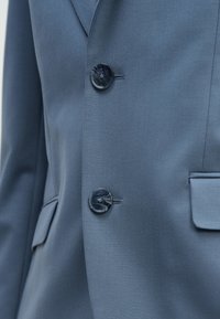 Világoskék blézer két fekete gombbal, éles hajtókával és oldalzsebbel, sima, texturált anyagból készült.