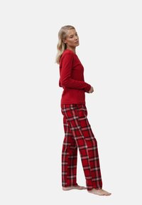 Top rojo de manga larga combinado con pantalones de cuadros rojos con acentos en negro y blanco. Tejido suave, corte relajado y diseño de largo completo.