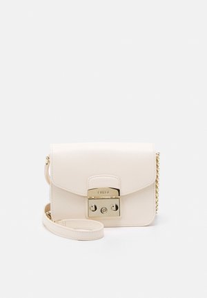 Petit sac bandoulière en cuir crème avec fermoir doré et détail de chaîne, forme rectangulaire, et bandoulière amovible, posé sur une surface blanche.