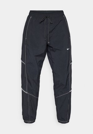 Schwarze Nylon-Jogginghosen mit elastischem Bund, Kordelzug und weißen Nähtelementen. Mit seitlichen Reißverschlusstaschen und einem Logo.