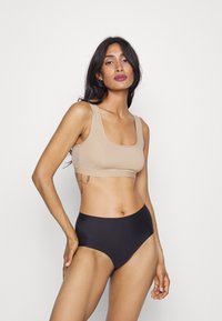 Beige ribbad crop top med breda axelremmar, parat med högmidjade svarta bikinibyxor. Den släta texturen och den åtsittande designen framhäver silhuetten.