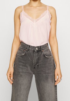 Jasnoróżowy top na cienkich ramiączkach z koronkową lamówką, o luźnym kroju, zestawiony z szarymi dżinsami z wysokim stanem.