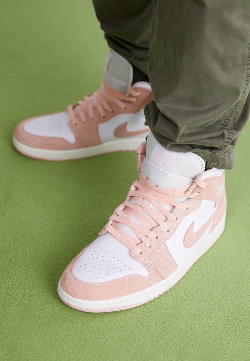 Baskets montantes avec une base en cuir blanc, des accents en daim rose, un bout perforé et des lacets texturés, sur fond vert.