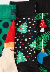 Τρία ζευγάρια με patterned κάλτσες: πράσινες με μαύρες κουκίδες και έναν νάνο, μαύρες με πολύχρωμες κουκίδες και δέντρα, και μαύρες με γιορτινές στολίδια και φύλλα.