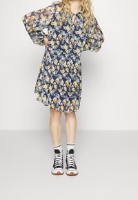 Květinové šaty s námořnickým pozadím, průhlednými dlouhými rukávy a volným střihem. Kombinované s černými vysokými teniskami a bílými kotníkovými ponožkami.